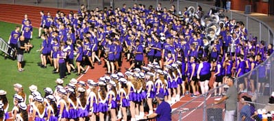 Photo of a large high school band all crowded at the end of the field waiting for halftime. 